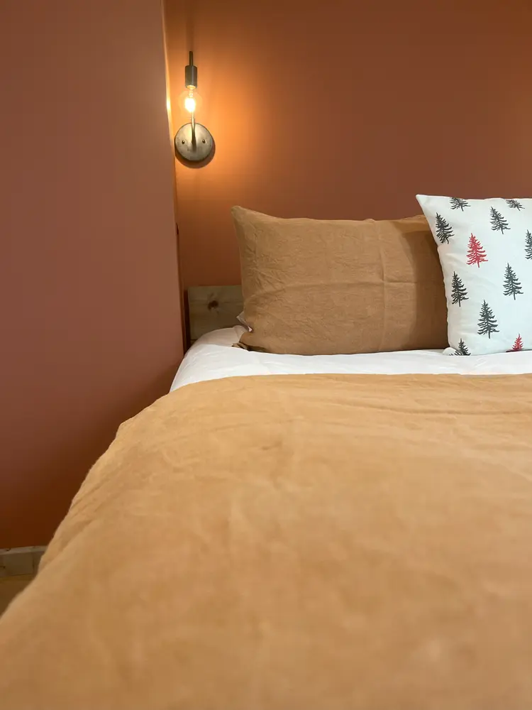 Detail of the bed in the Fougère room: ochre bedspread, cushions and wall light on a terracotta wall