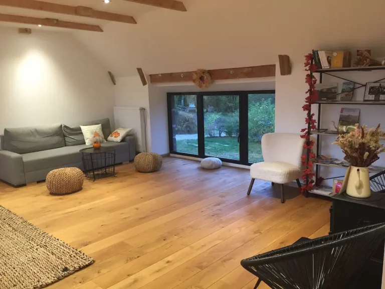 Le salon commun : canapé gris, poufs, fauteuil blanc moelleux et grande baie vitrée sur le jardin