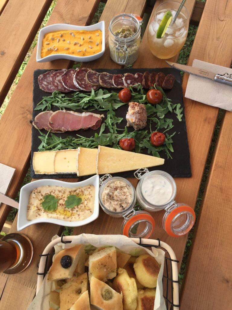 Planche de charcuteries, fromages et focaccia posée sur une table en bois, avec une boisson fraîche