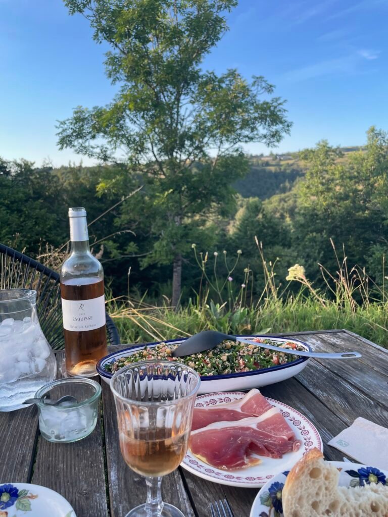 Aperitif im Freien: eine Flasche Rosé, ein Glas und ein Teller Schinken mit Blick auf das Tal