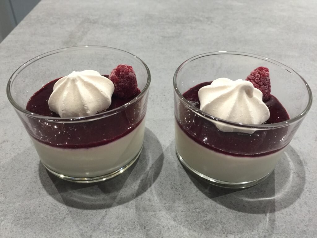Deux verrines de dessert : crème blanche, coulis de fruits rouges, meringue et framboise