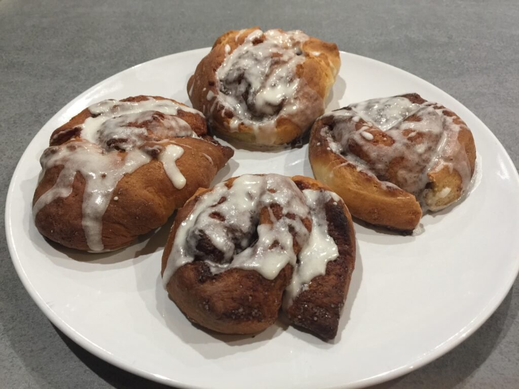 Quatre brioches roulées glacées servies sur une assiette blanche
