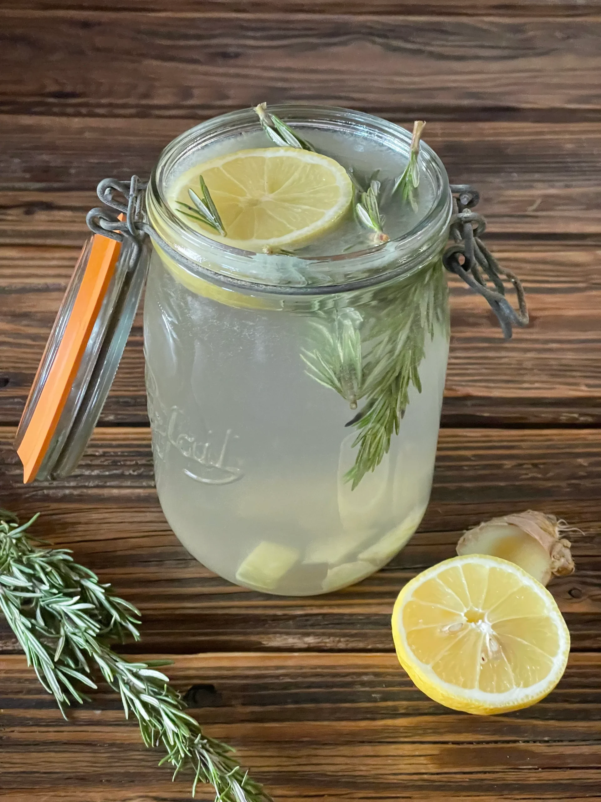 Glas Zitronenlimonade mit Zitrone und Rosmarin auf einem Holztisch