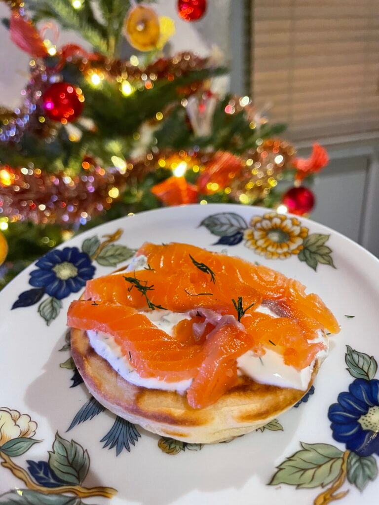 Blini au saumon fumé et à l’aneth sur une assiette fleurie, devant un sapin de Noël décoré