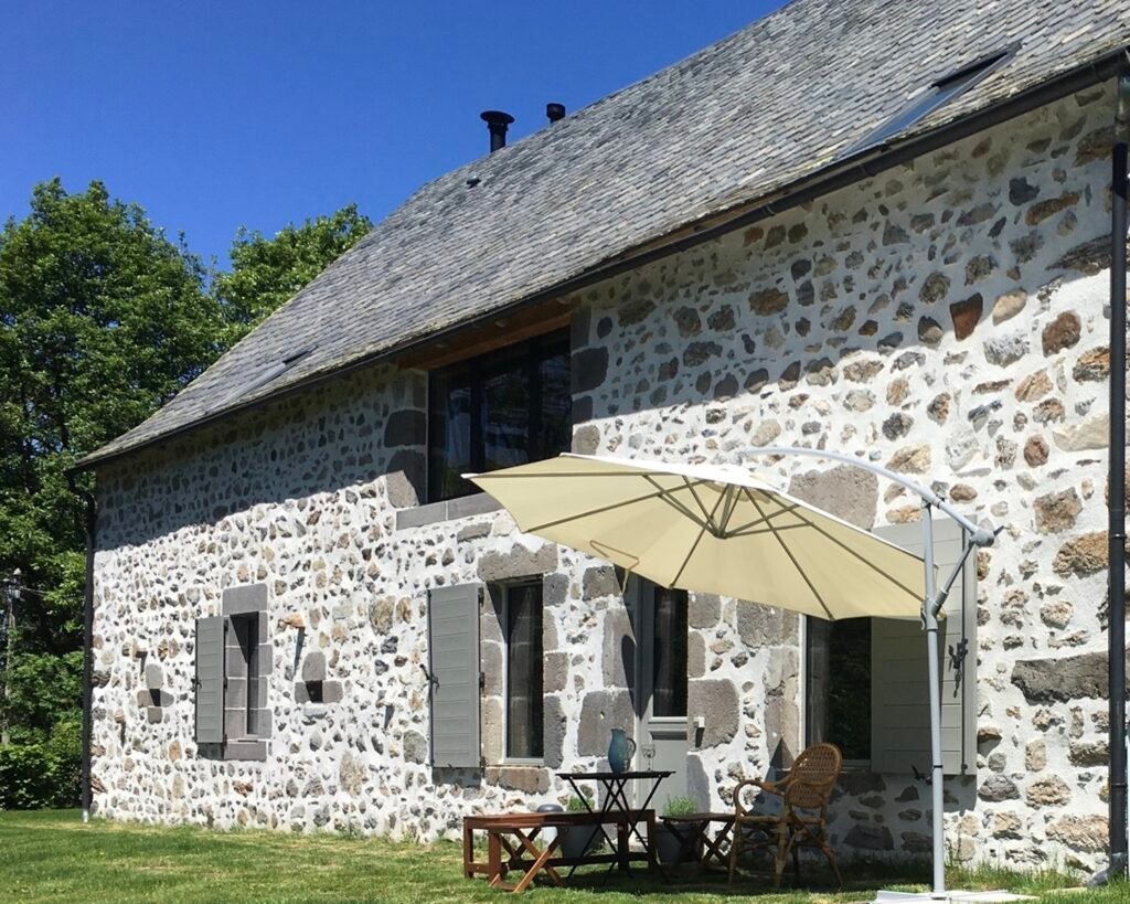 Die Steinfassade von La Grange de L’Abille mit Sonnenschirm, Tisch und Stühlen im Garten