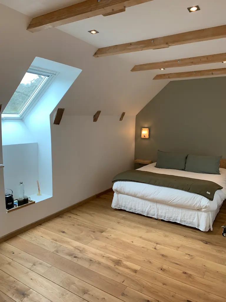 La chambre Bruyère : lit sous les poutres, mur vert sauge et fenêtre de toit