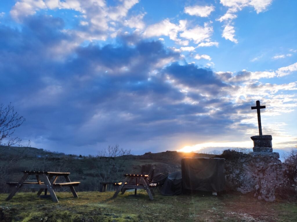 Das Steinkreuz und die Picknicktische bei Sonnenuntergang, unter einem großen wolkigen Himmel