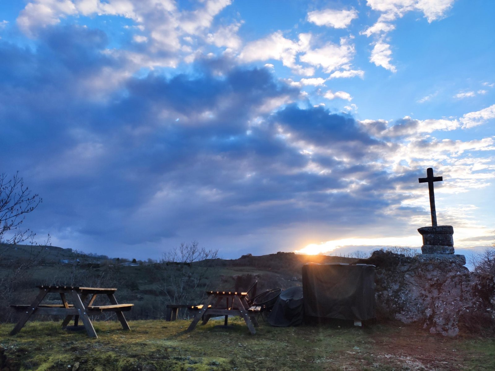 The stone cross and the picnic tables at sunset, under a big cloudy sky
