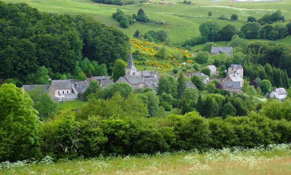 The village of Marchastel: the bell tower and the stone roofs among meadows, woods and flowering broom