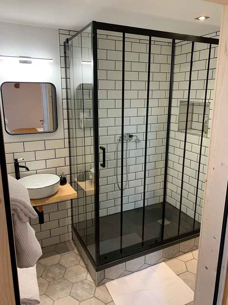 Salle de bain de la chambre Fougère : douche vitrée à cadre noir et carrelage blanc
