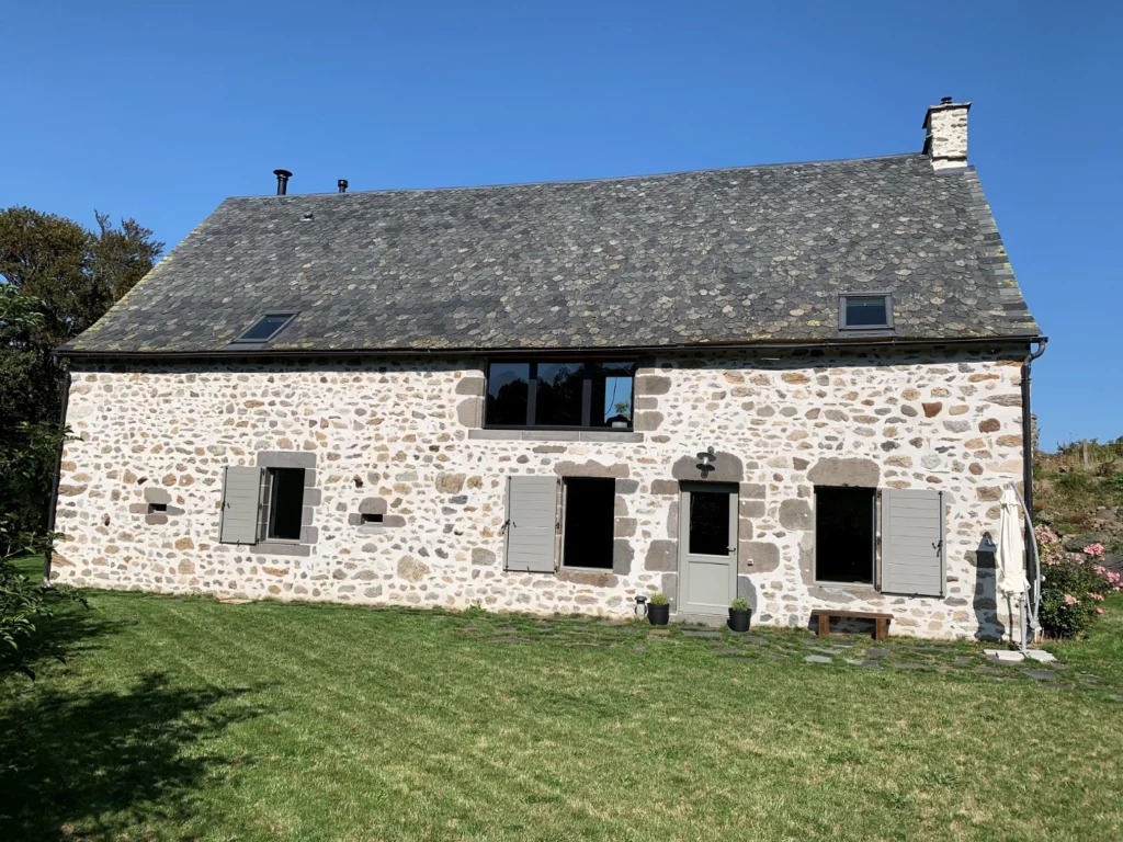 Stone façade of La Grange de L'Abille, grey shutters and lawn