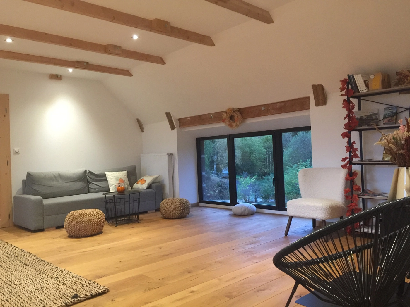 Le salon commun aux deux chambres : canapé, grande baie vitrée, poutres apparentes et plancher en chêne