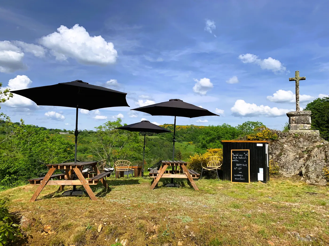 Terrasse de La Grange de L'Abille, parasols et tables face à la croix de pierre