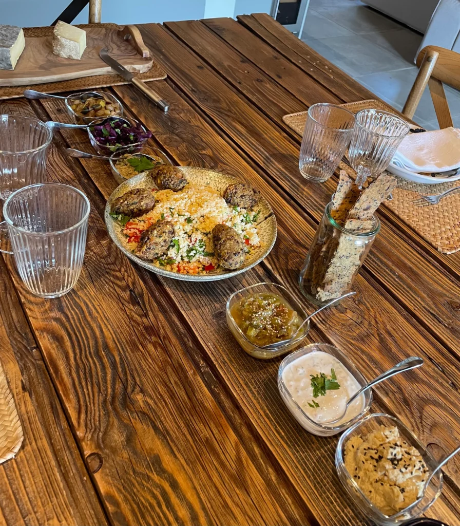 Plats variés et petites coupelles de sauces sur une table en bois, avec des verres cannelés